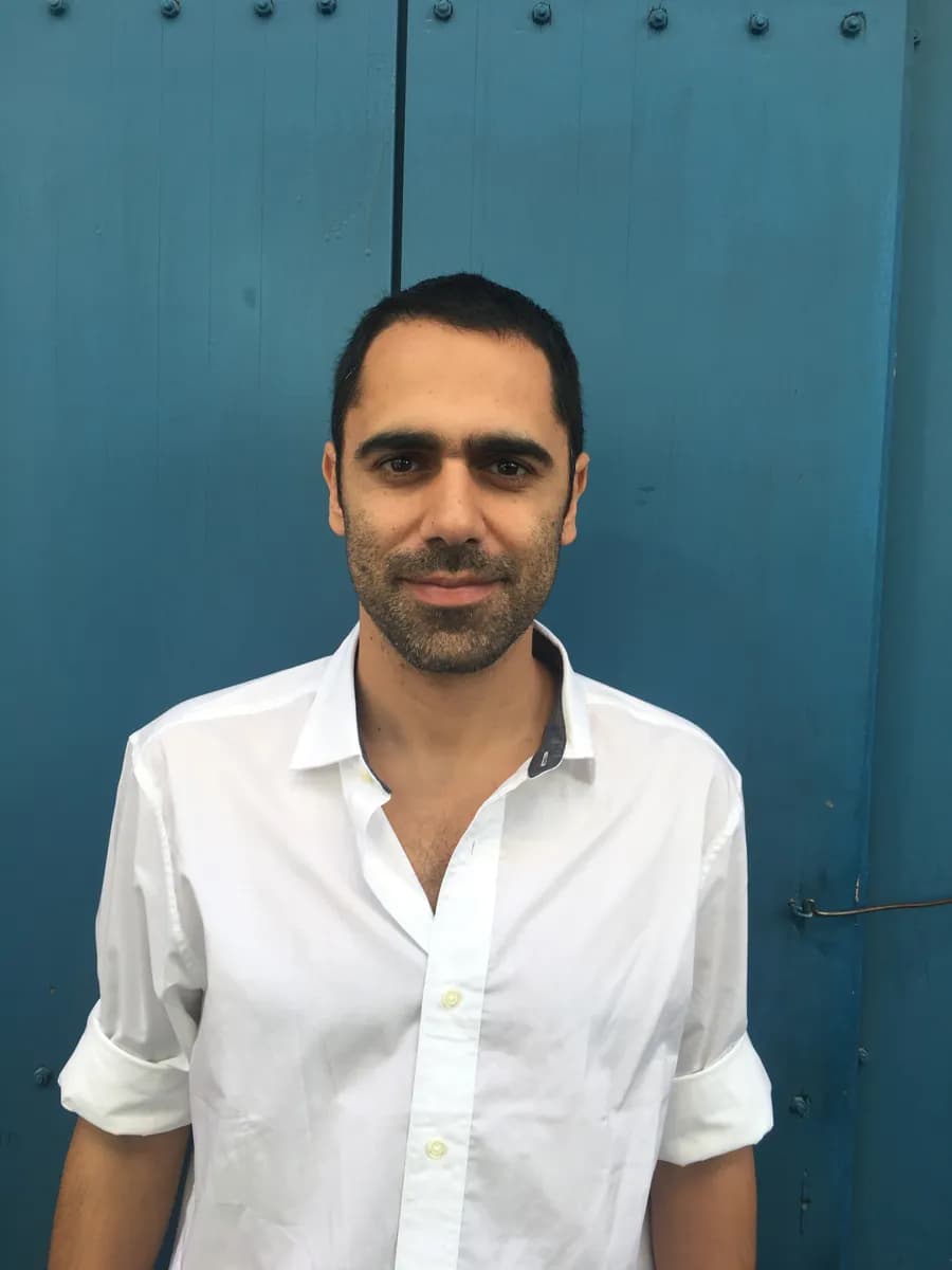 Sinay in a white shirt, standing in front of a blue wooden door